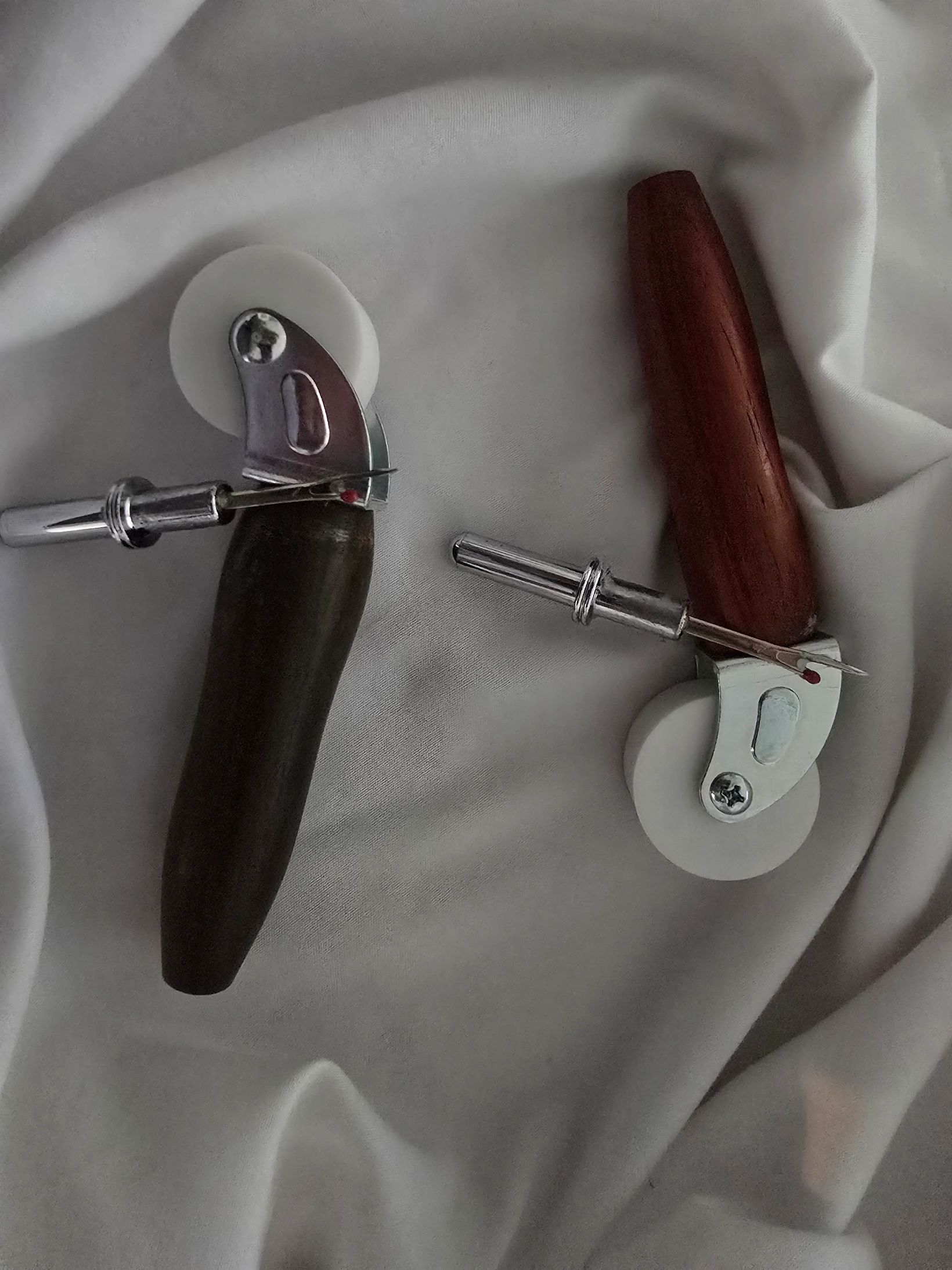 Two pizza cutters with wooden handles on white fabric